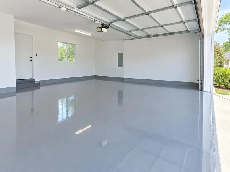 Garage vide aux murs blancs avec sol en résine époxy gris brillant et porte sectionnelle.