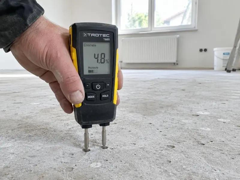 Mesure du taux d’humidité d’une dalle de béton brut avec un humidimètre à pointes à affichage numérique.